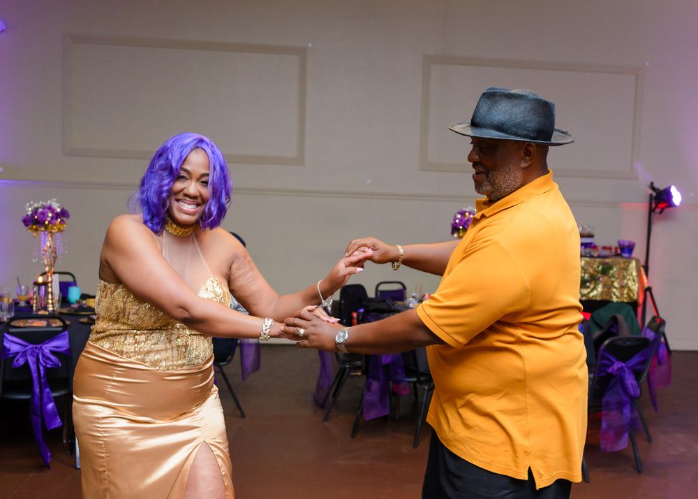 People dancing together in pairs at a celebration with purple lighting and decor.