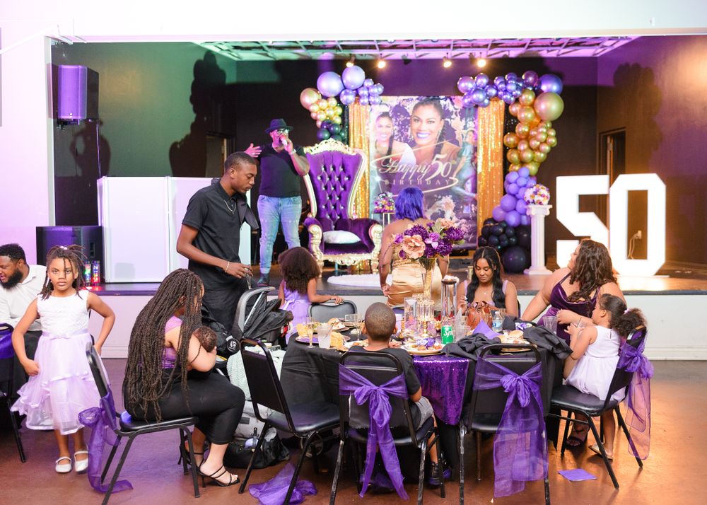 Wide view of an event space with purple lighting and guests seated at round tables.