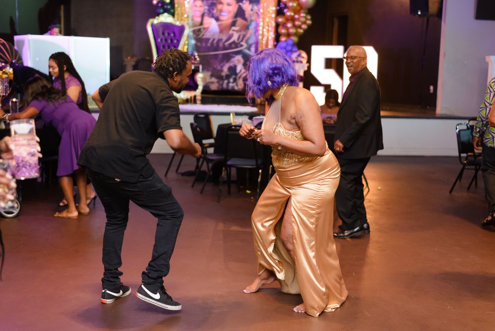People dancing together at a festive event with purple lighting and decorative elements in the background.