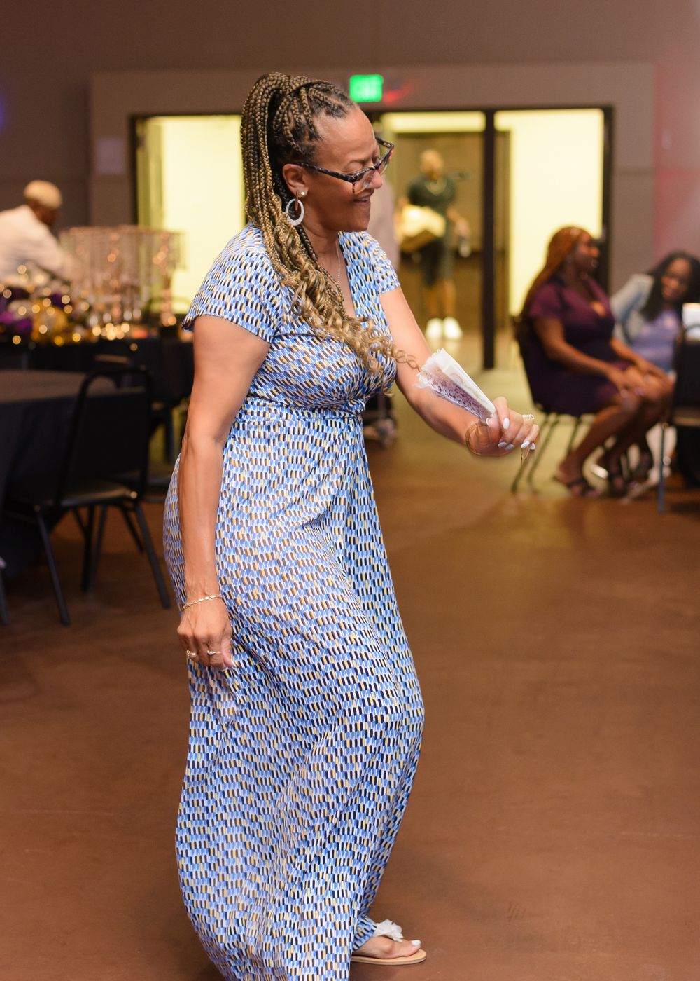 Person in a blue patterned dress twirling on a dance floor at an indoor event.