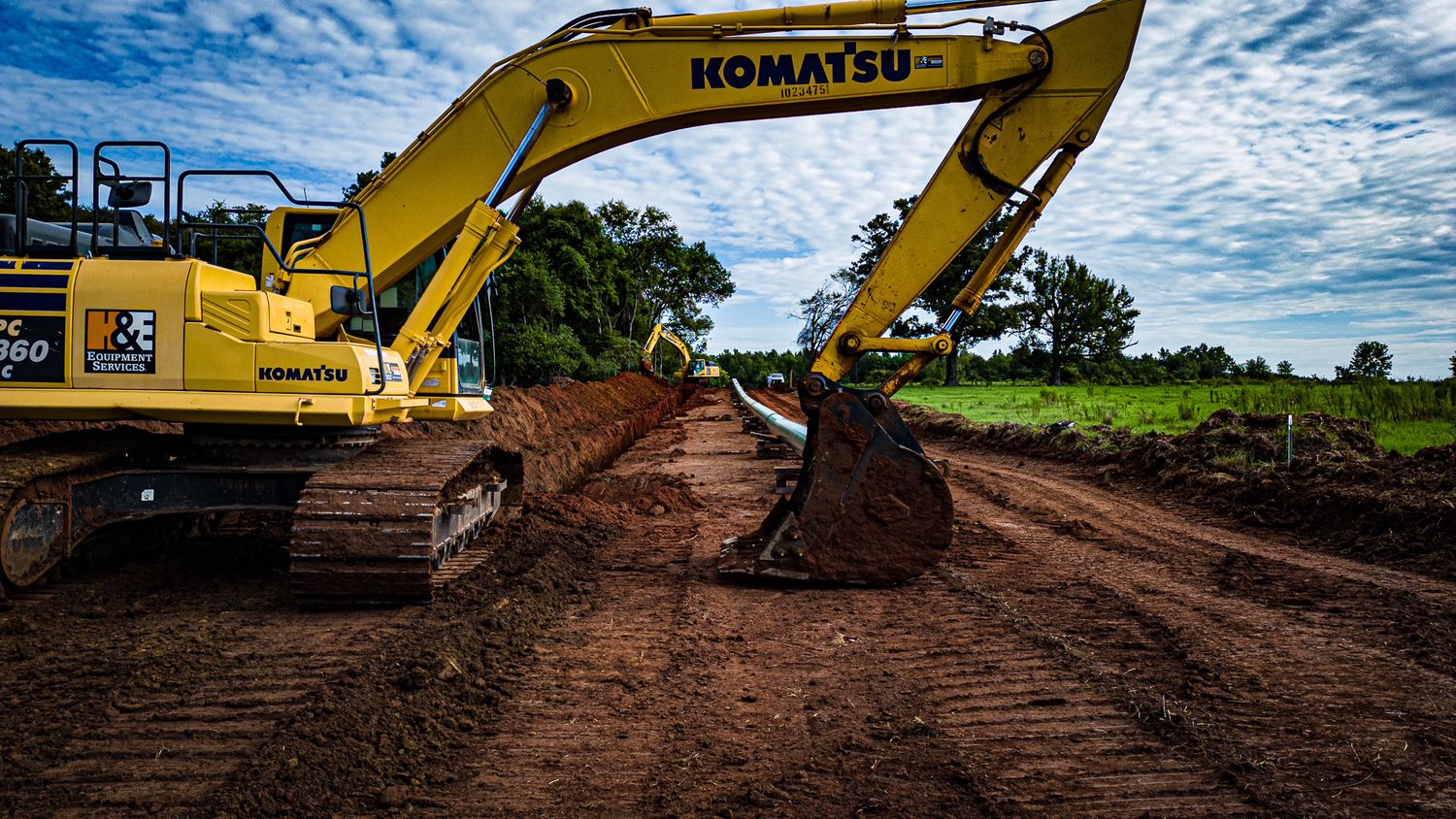 Yellow excavator with extended arm performing earthwork operations at a construction site under cloudy skies.