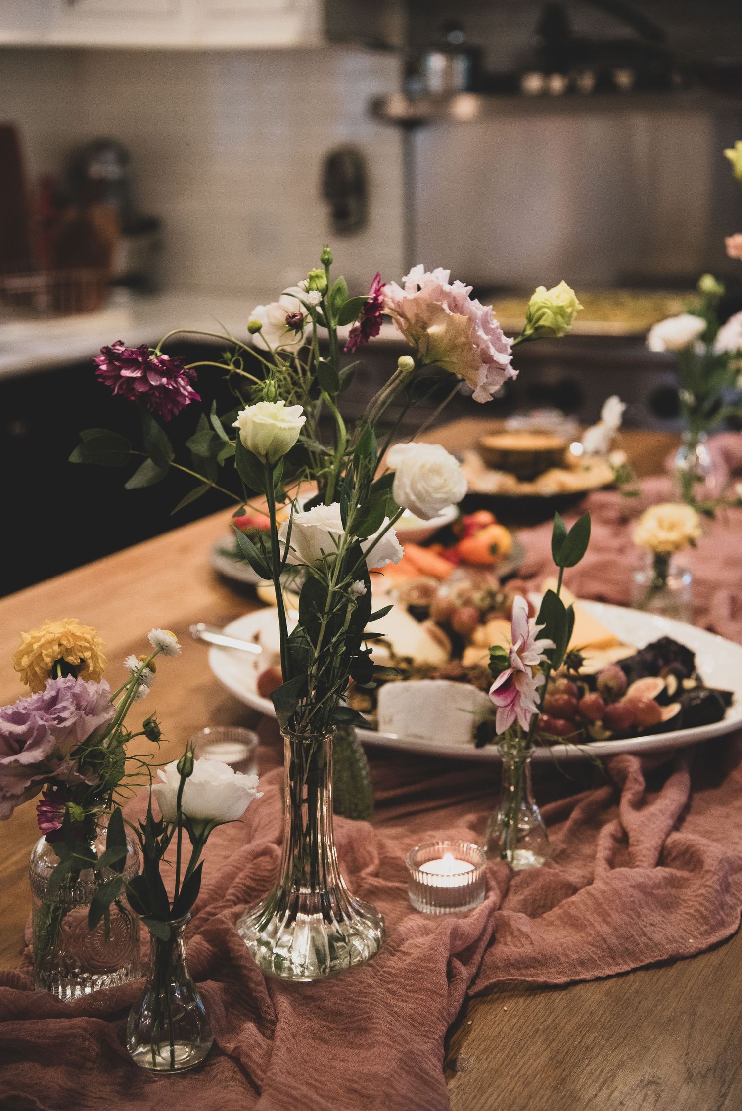 Romantic table setting with small vases of pink flowers and candles on a rustic wooden surface.