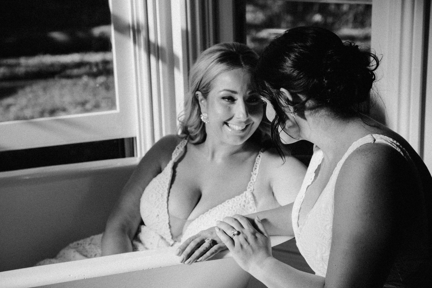 A tender black and white moment between two people sharing a laugh while sitting near a window.
