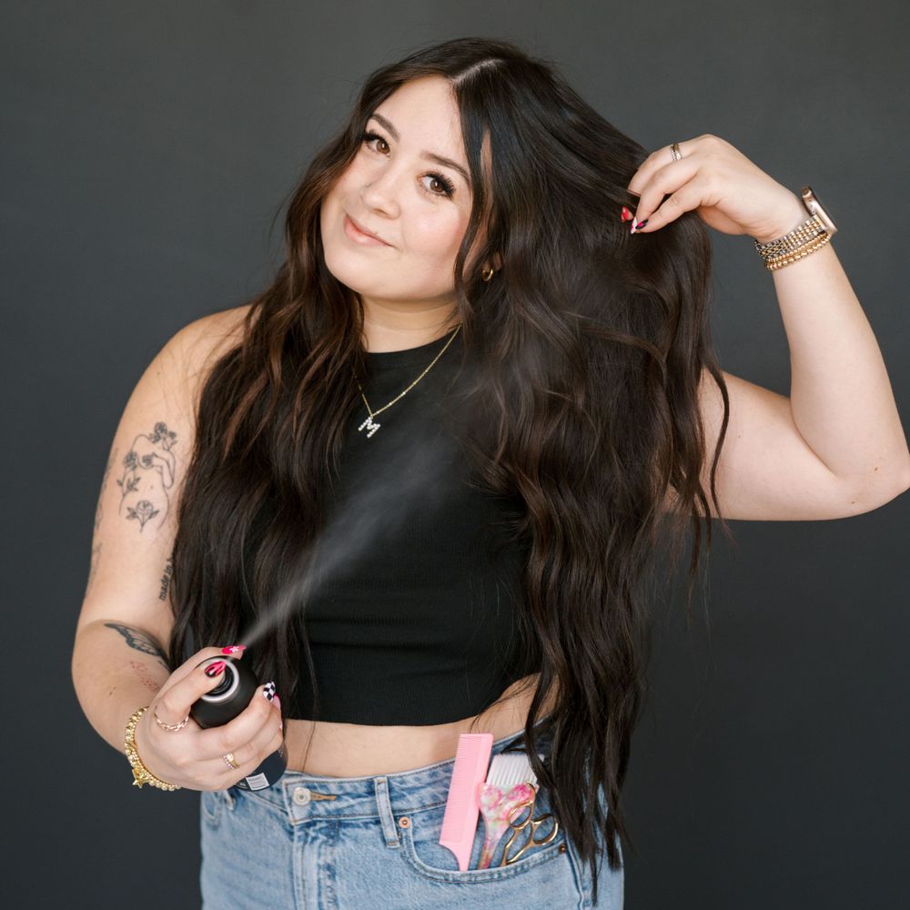 Person with long dark hair in black crop top poses against dark background.