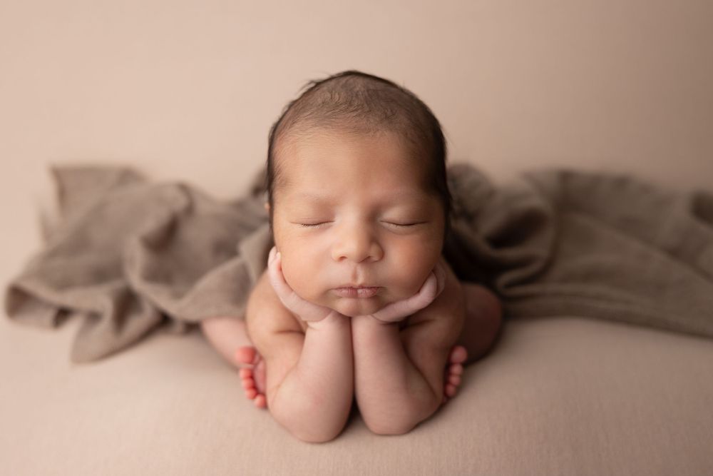 Sleeping newborn resting head on hands on beige backdrop with soft brown fabric.