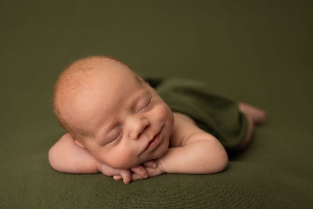 Sleeping newborn baby lying on dark green blanket in multiple artistic poses.