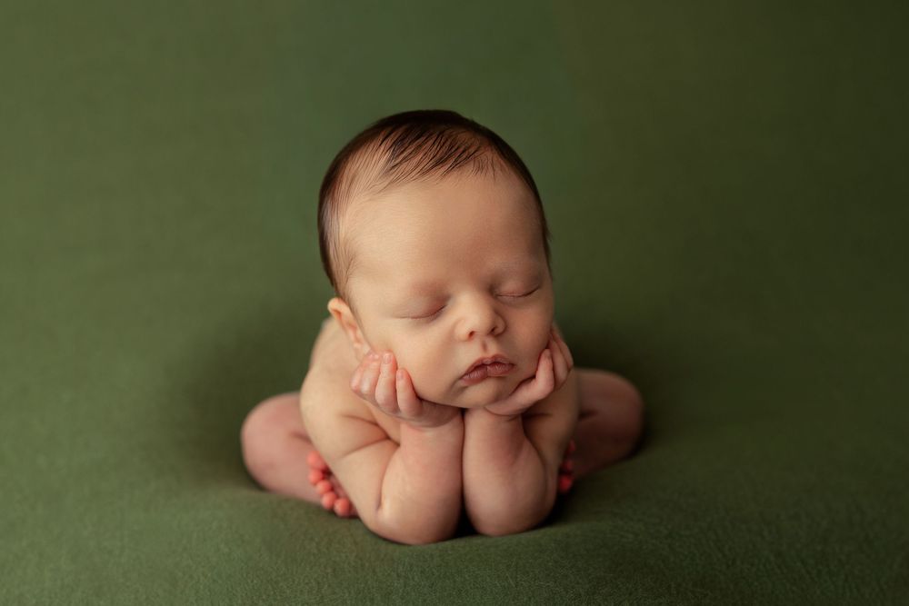 A sleeping newborn baby lies curled up on a soft green backdrop in an artistic portrait series. Colorado Springs newborn photography.