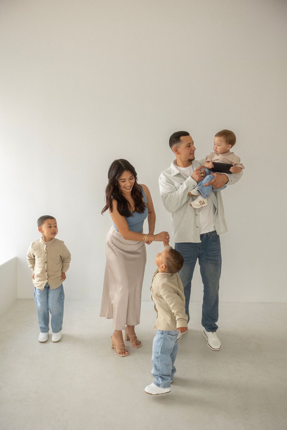 A family of five poses together against a plain white wall in a minimalist studio setting.
