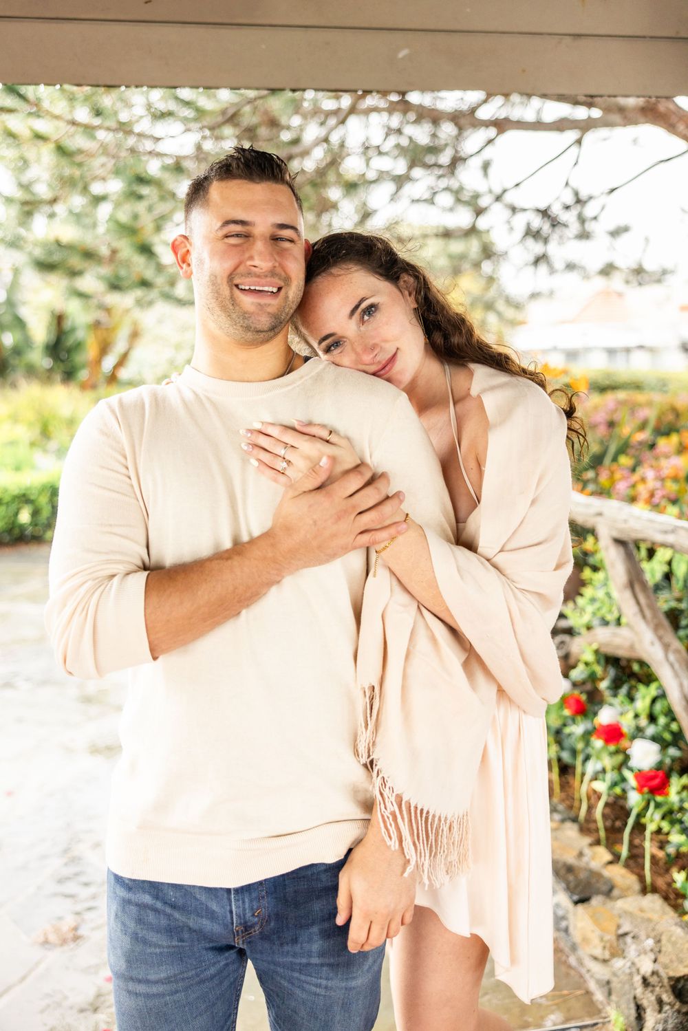 Couple in light colored clothing sharing tender moment on garden porch.