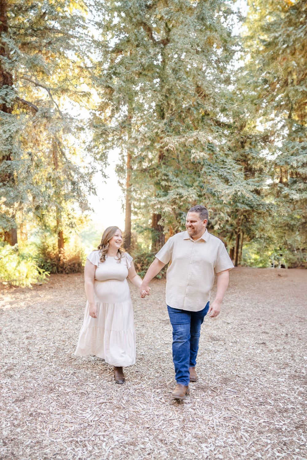 Couple walking hand in hand through a wooded path during golden hour.