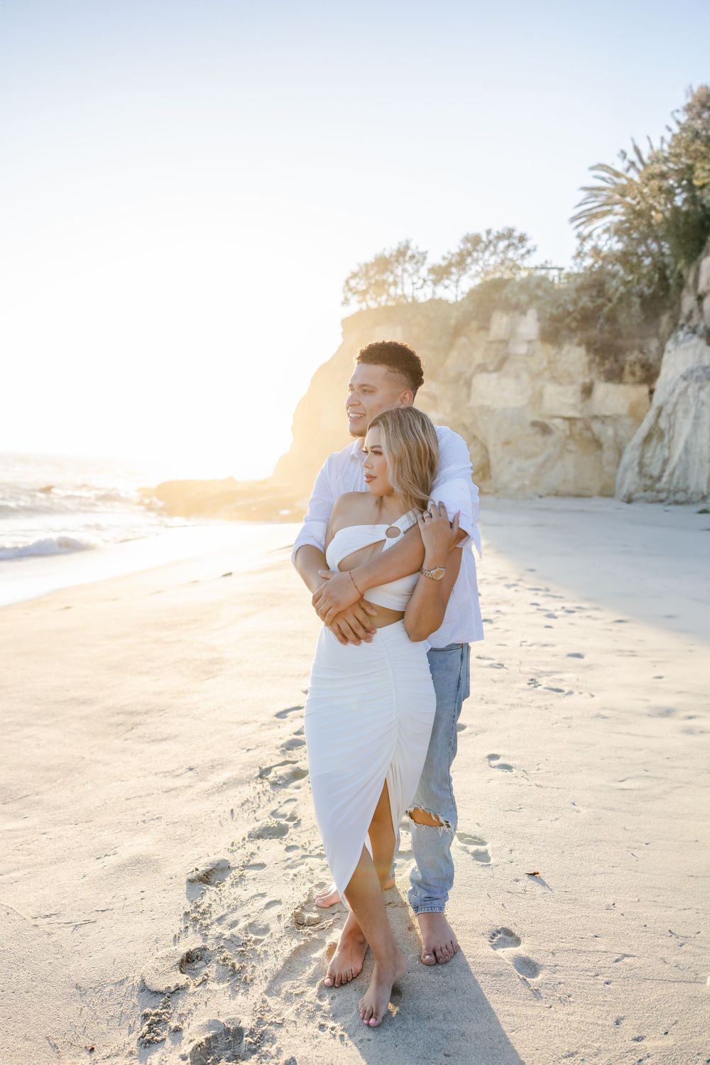 A couple embraces on a sandy beach during sunset.