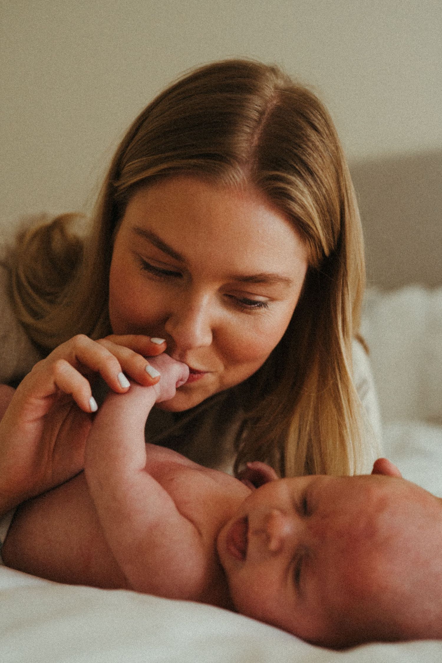 A tender moment between parent and newborn baby lying together on white bedding.