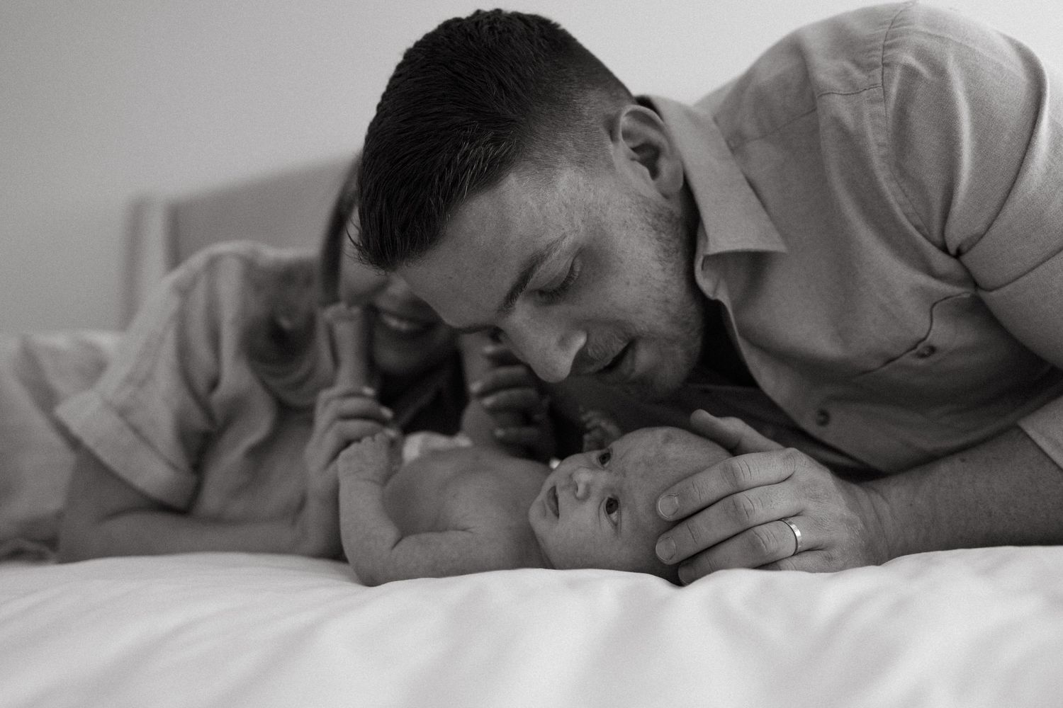 Intimate black and white portrait of family members sharing affectionate moments on bed.