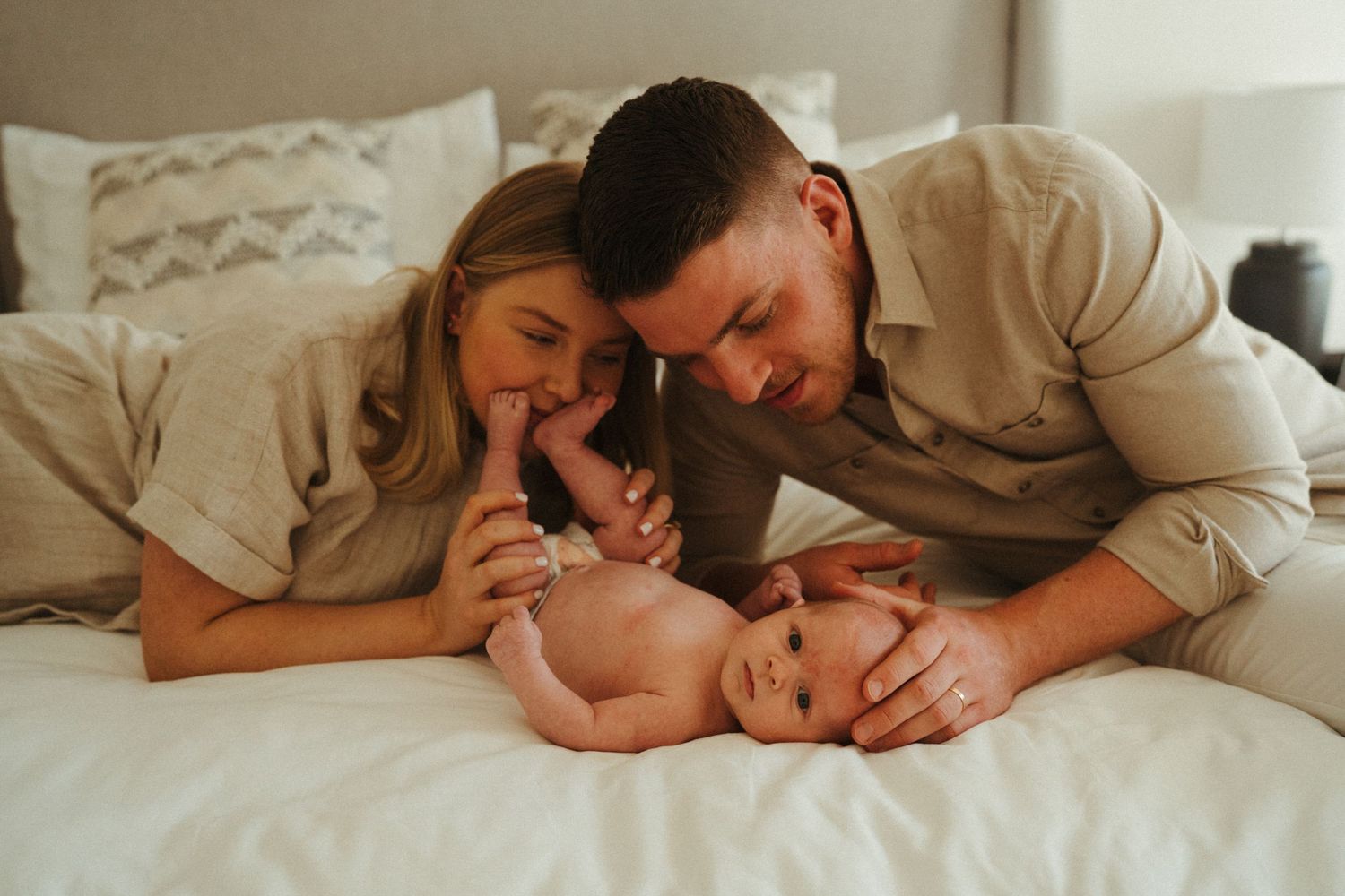 Loving family cuddles together on white bedding in a series of candid shots.