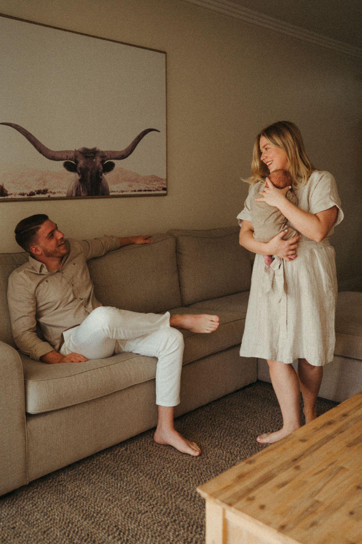 Intimate family photoshoot with people in white clothing sharing loving moments on a beige couch.