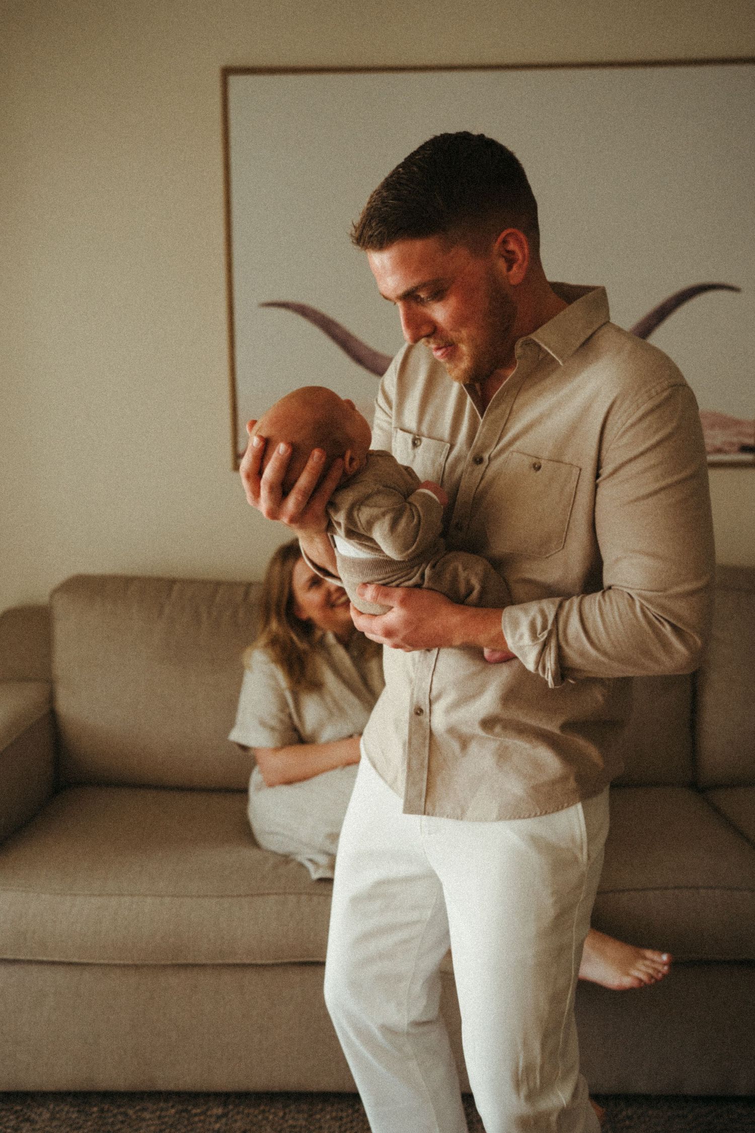 Couple sitting together on a grey couch in matching beige outfits.
