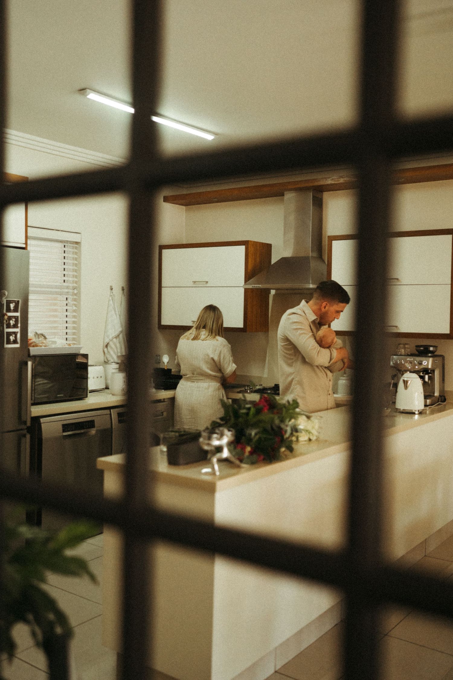 Kitchen interior viewed through window bars showing white countertops and modern appliances.