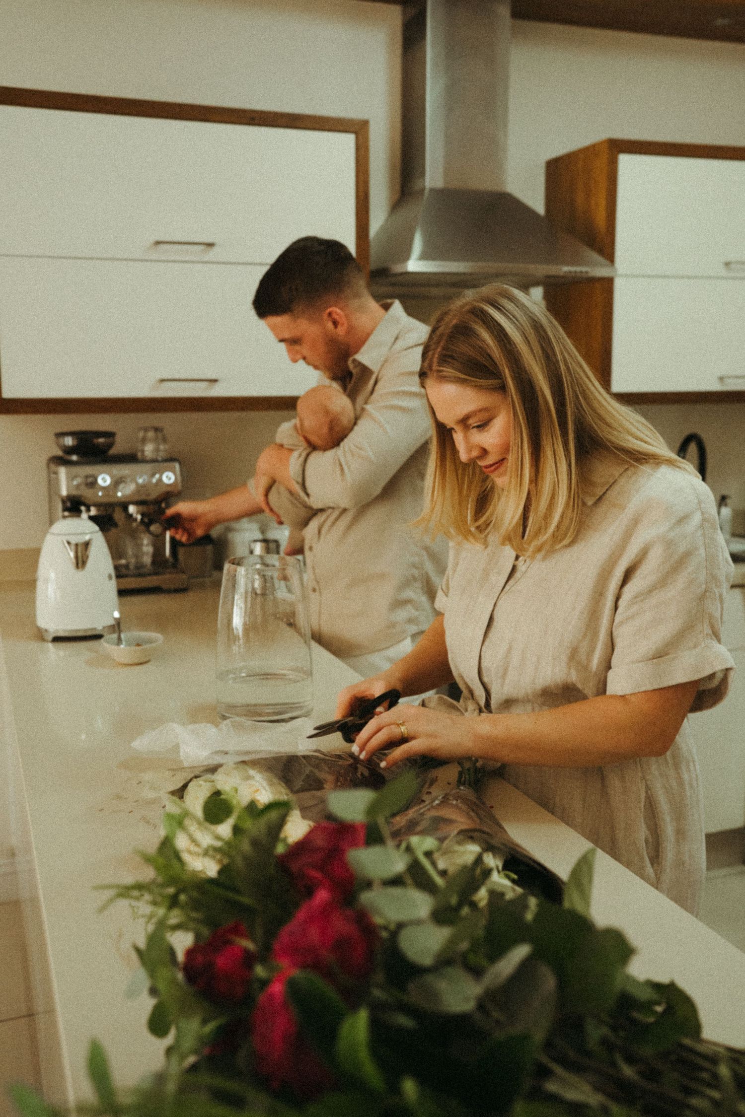 Modern kitchen scene with red flowers in vase on white countertop.