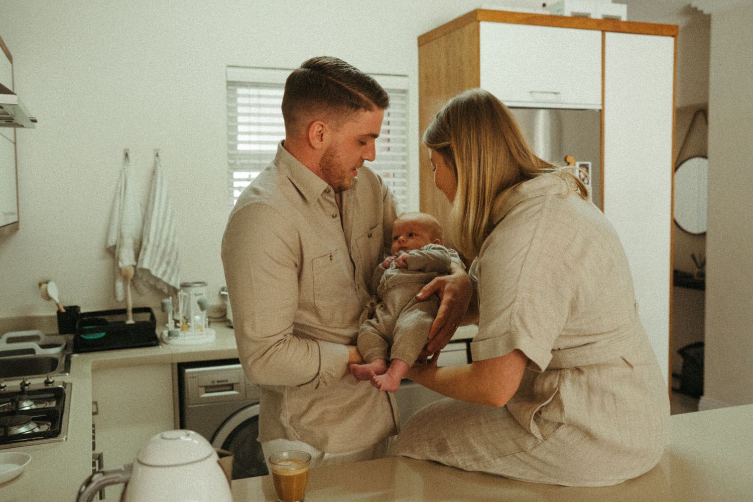 Couple in matching beige outfits sitting together in modern kitchen.