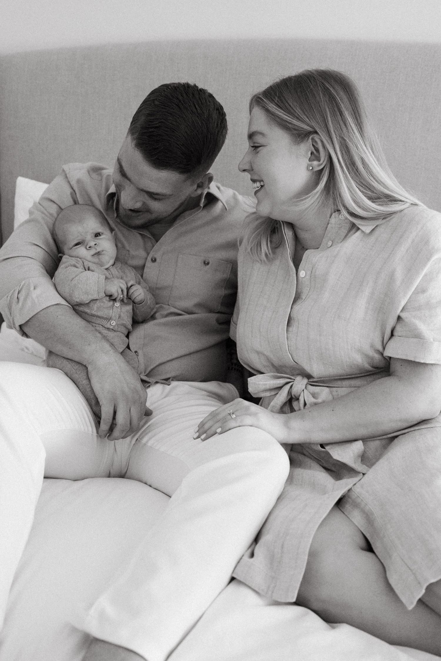 Black and white lifestyle photography of family relaxing together on white bedding.