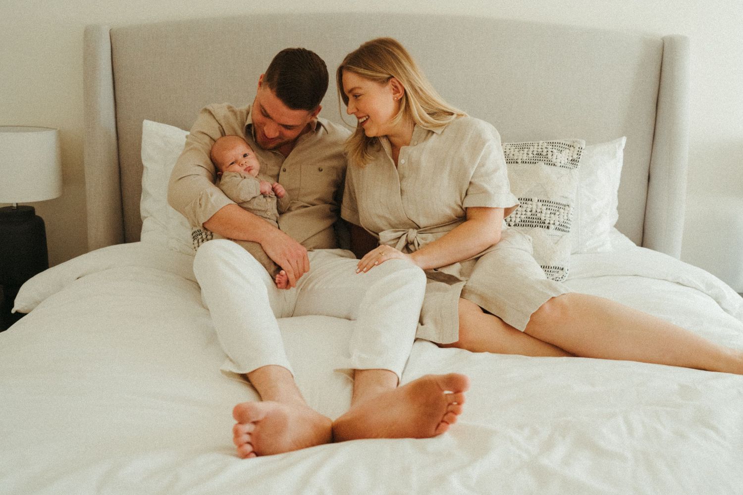 Panoramic family portrait showing tender moments on a white bed.