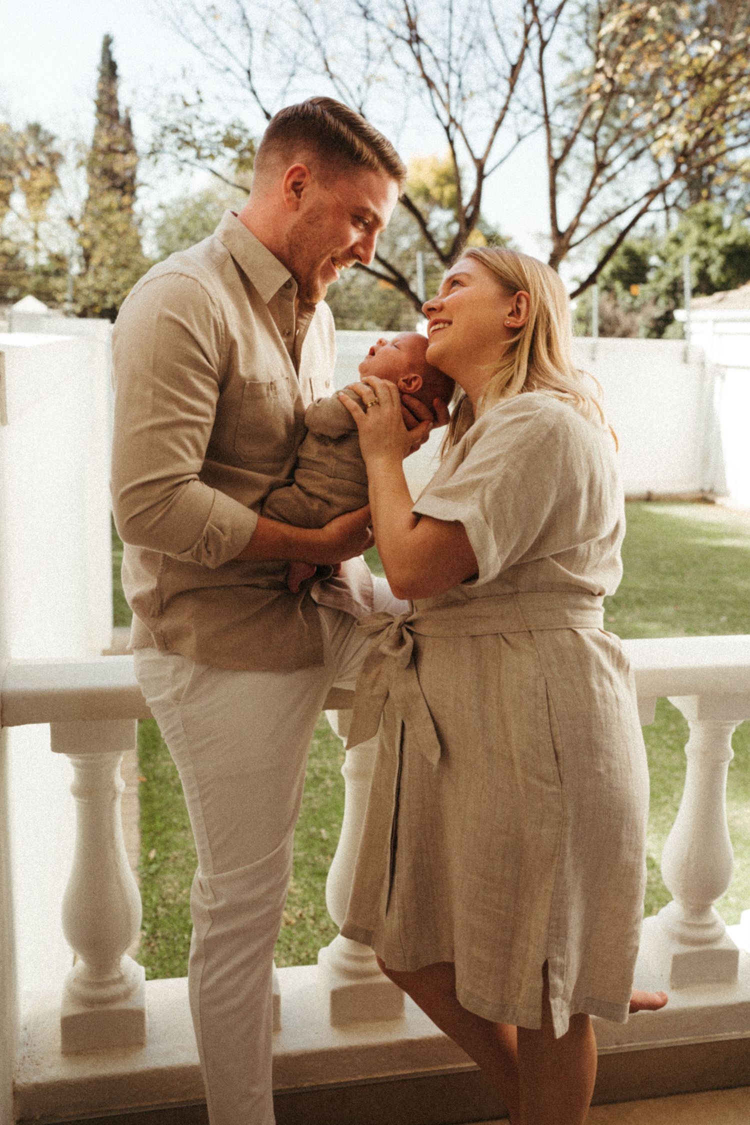 Sun-lit outdoor family portrait session on a white balcony with natural backdrop.