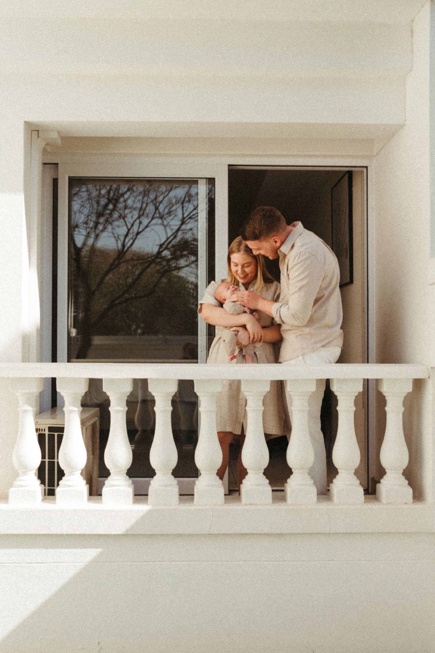 Couple in matching light outfits share intimate moments along a white balcony with decorative balusters.