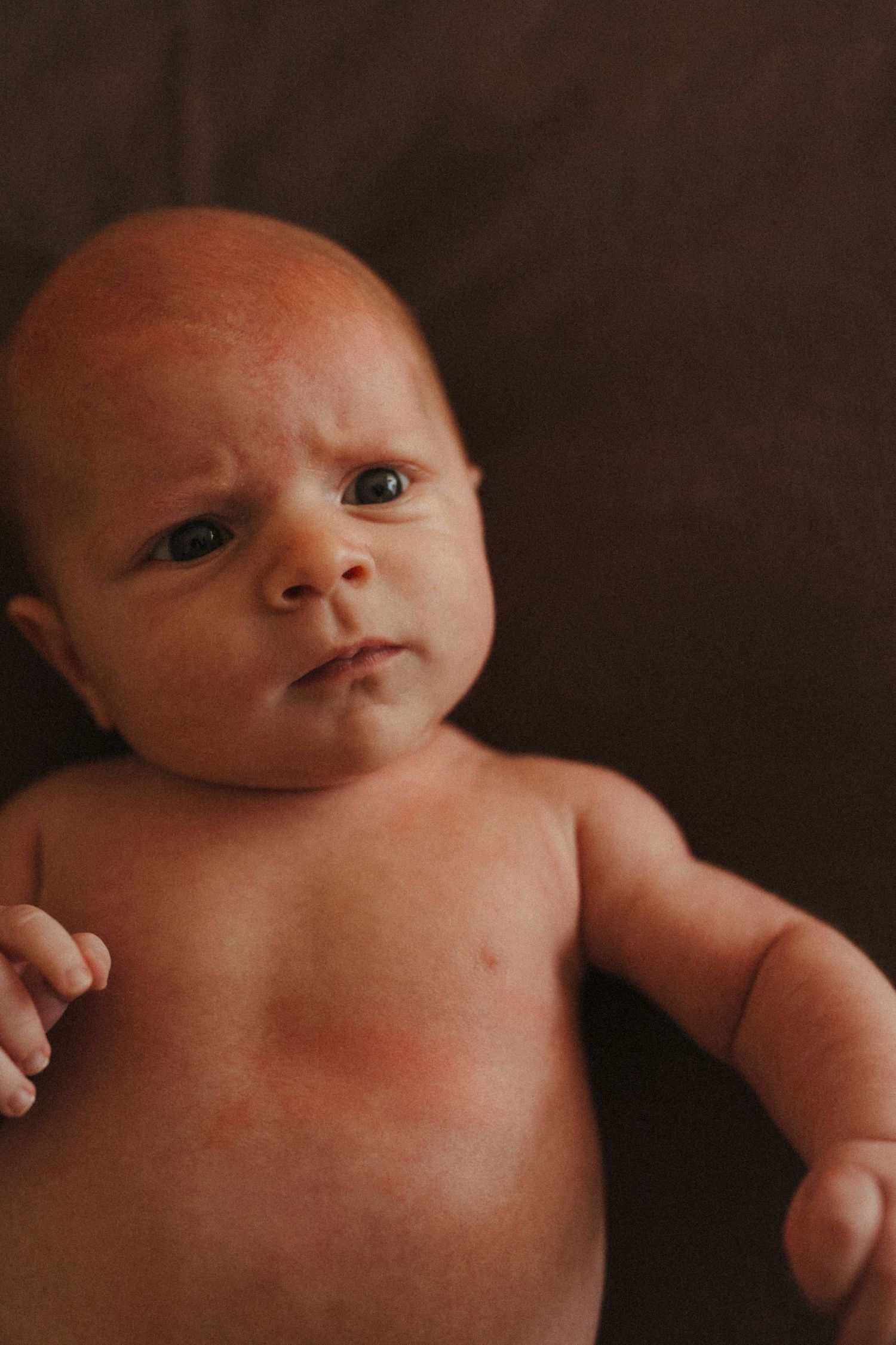Close-up portraits of a newborn baby in moody lighting against a dark background.