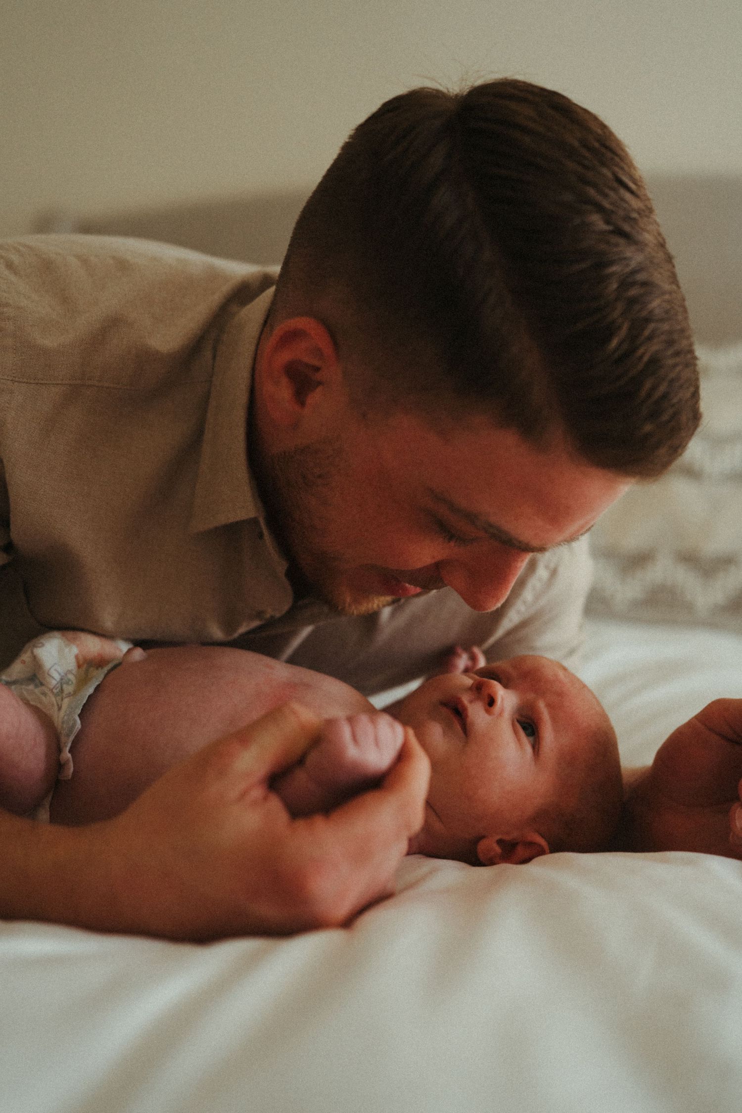 Parent sharing gentle nose-to-nose moment with newborn on white sheets.