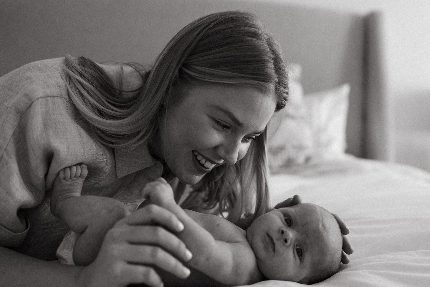 Mother tenderly bonding with newborn baby on white bedding.