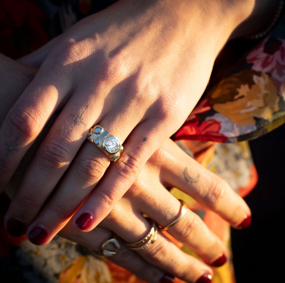 Closeup of hands with engagement ring and red nail polish in soft lighting.