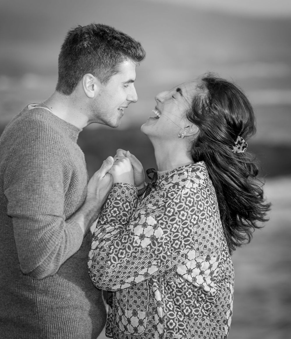 A romantic black and white photo series of a couple embracing on a beach with wind blowing through their hair.