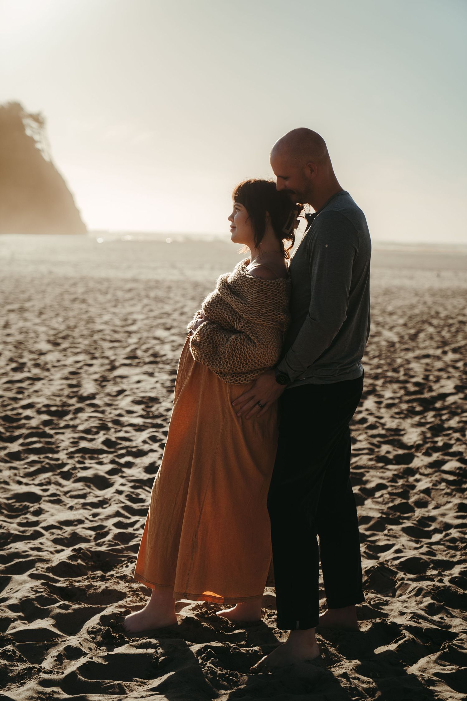 Romantic couple embracing on a sandy beach at golden hour with ocean waves in the background.