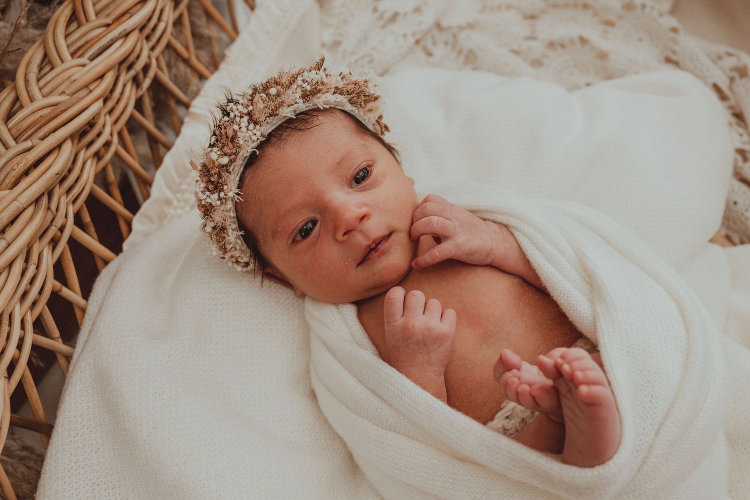 Newborn baby sleeping peacefully in woven basket with soft white blanket next to piano keys.