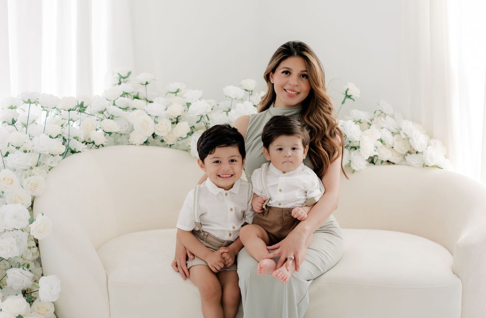 Elegant family photo on white couch with floral backdrop in light neutral tones and coordinated outfits.