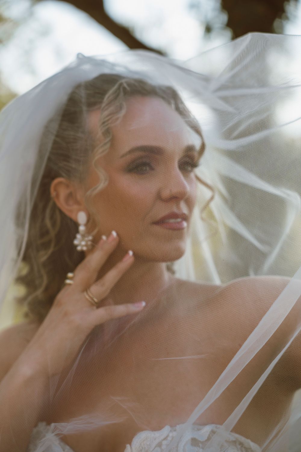 Ethereal bridal portrait with soft lighting and flowing veil showing elegant jewelry.