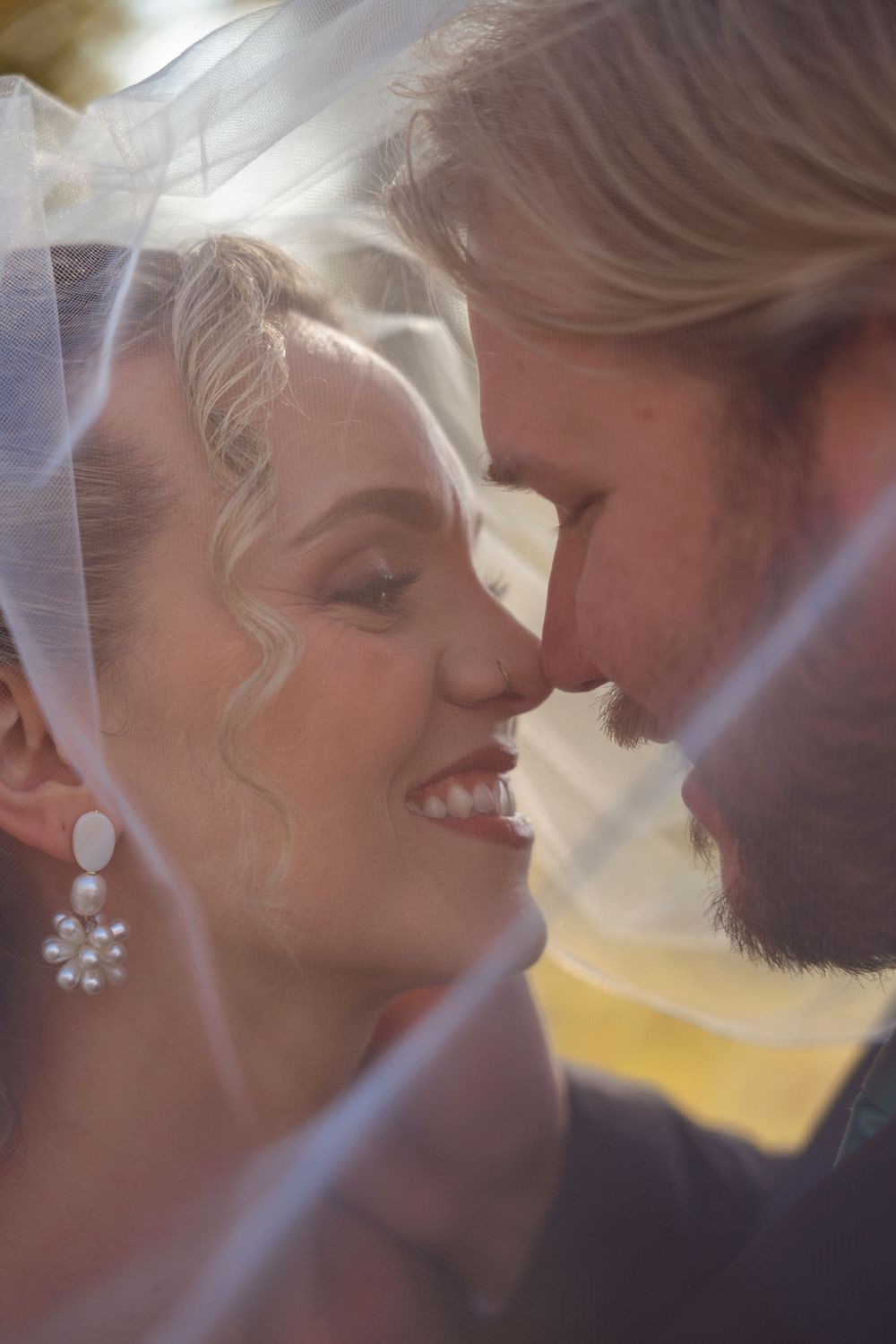 Intimate romantic moment captured between newlyweds under a flowing white veil.