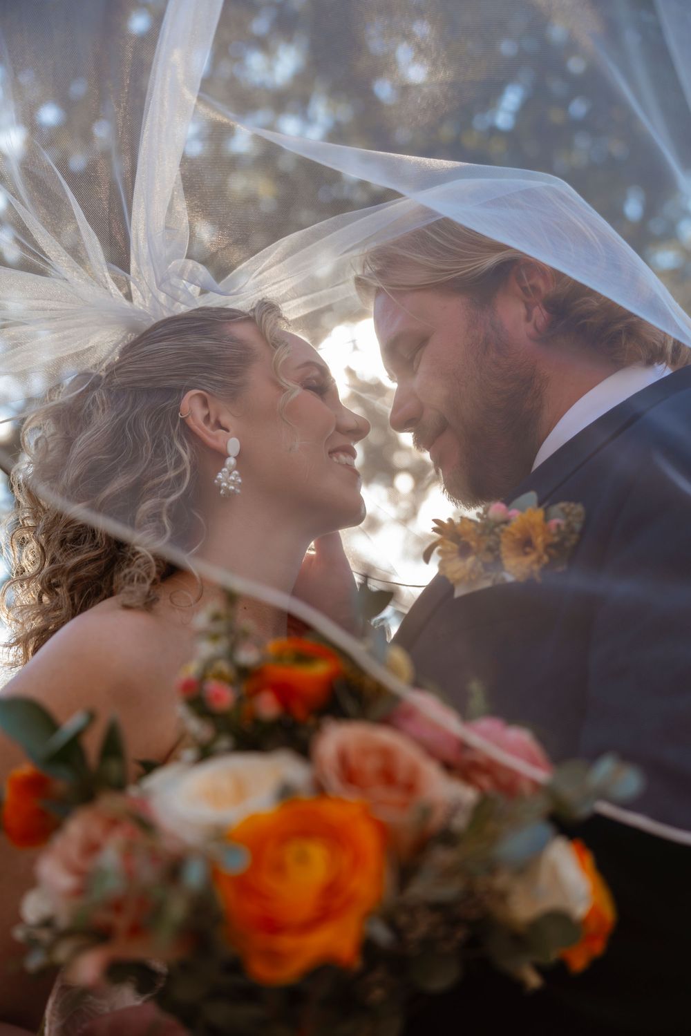 Romantic wedding portrait with colorful bouquet of orange flowers in soft sunlight.