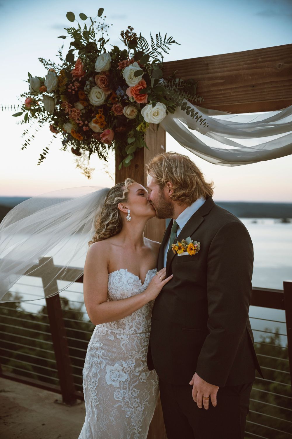 A couple shares a tender moment at their outdoor wedding with ocean views and floral arch decorations.