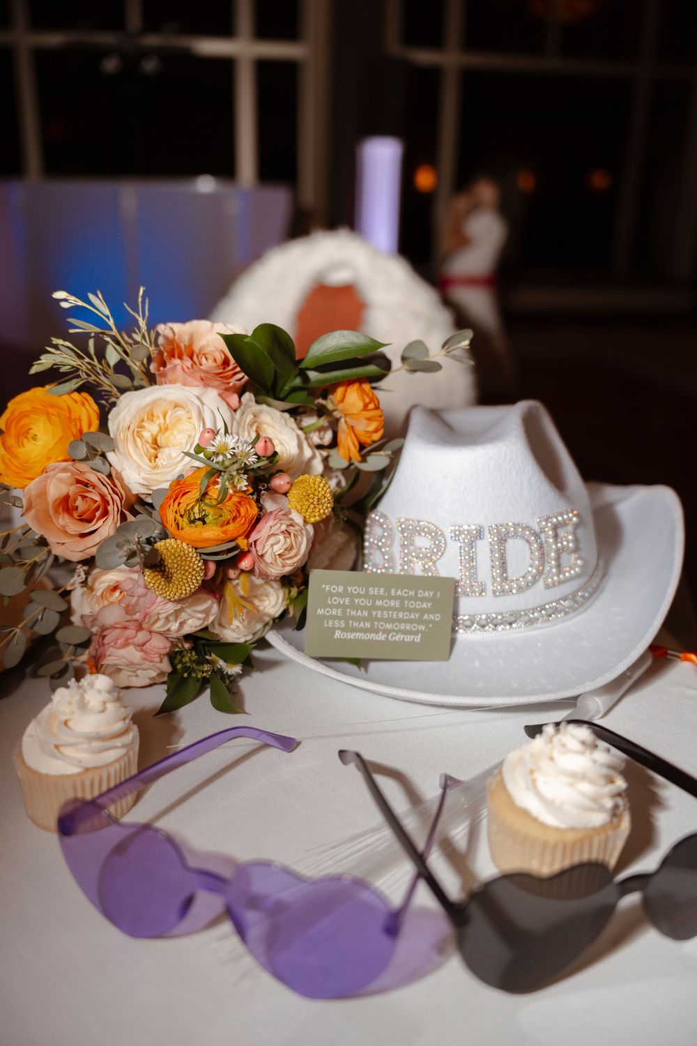 Wedding reception table with cupcakes, floral arrangements, and decorative 'Bride' sign.