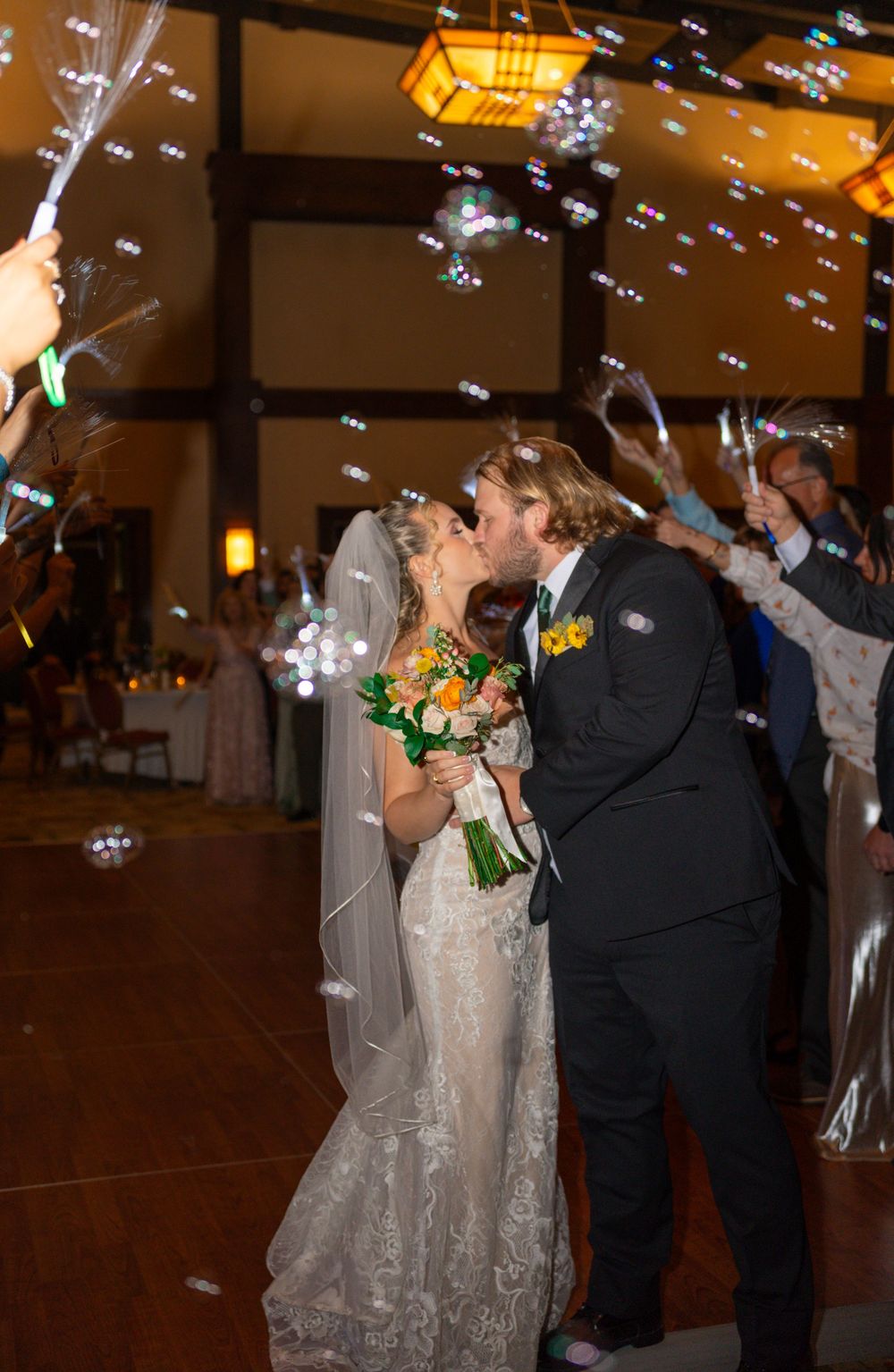 Wedding celebration with bubbles floating around the couple during an indoor evening reception.