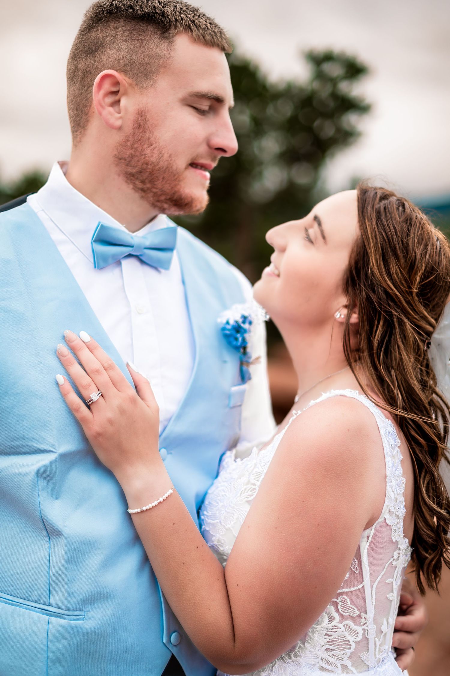 A couple shares a romantic moment at their wedding, with the groom in a light blue vest and the bride in white lace.