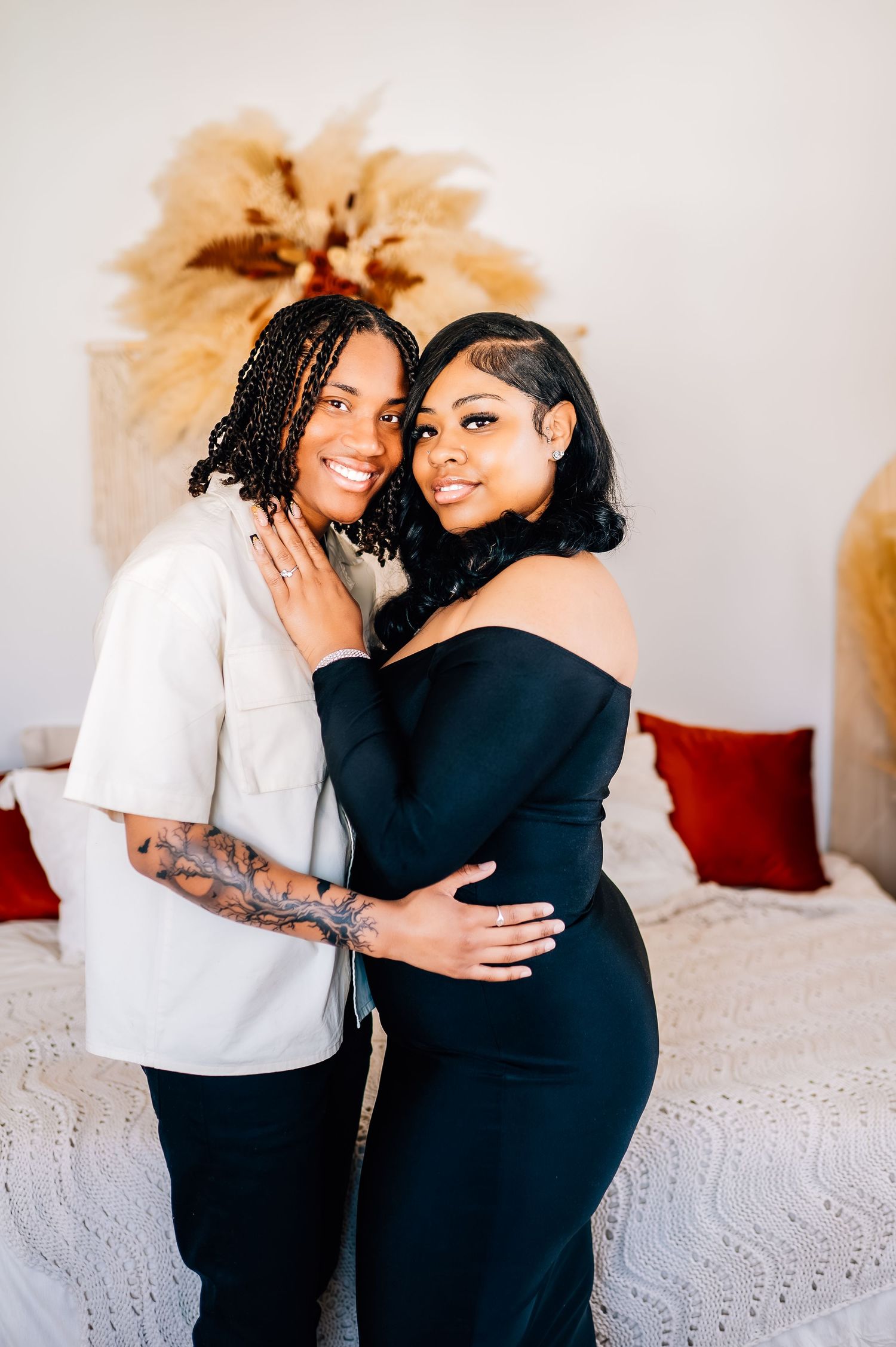 Two people embrace in a cozy indoor setting with dried pampas grass decor in the background.