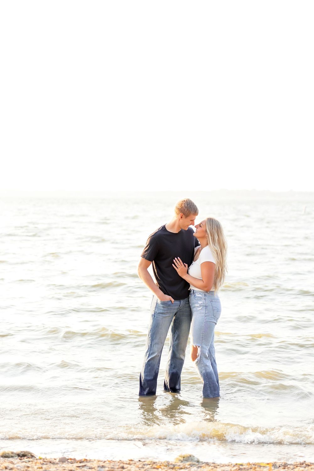 Romantic couple stands in shallow water at the beach during sunset.
