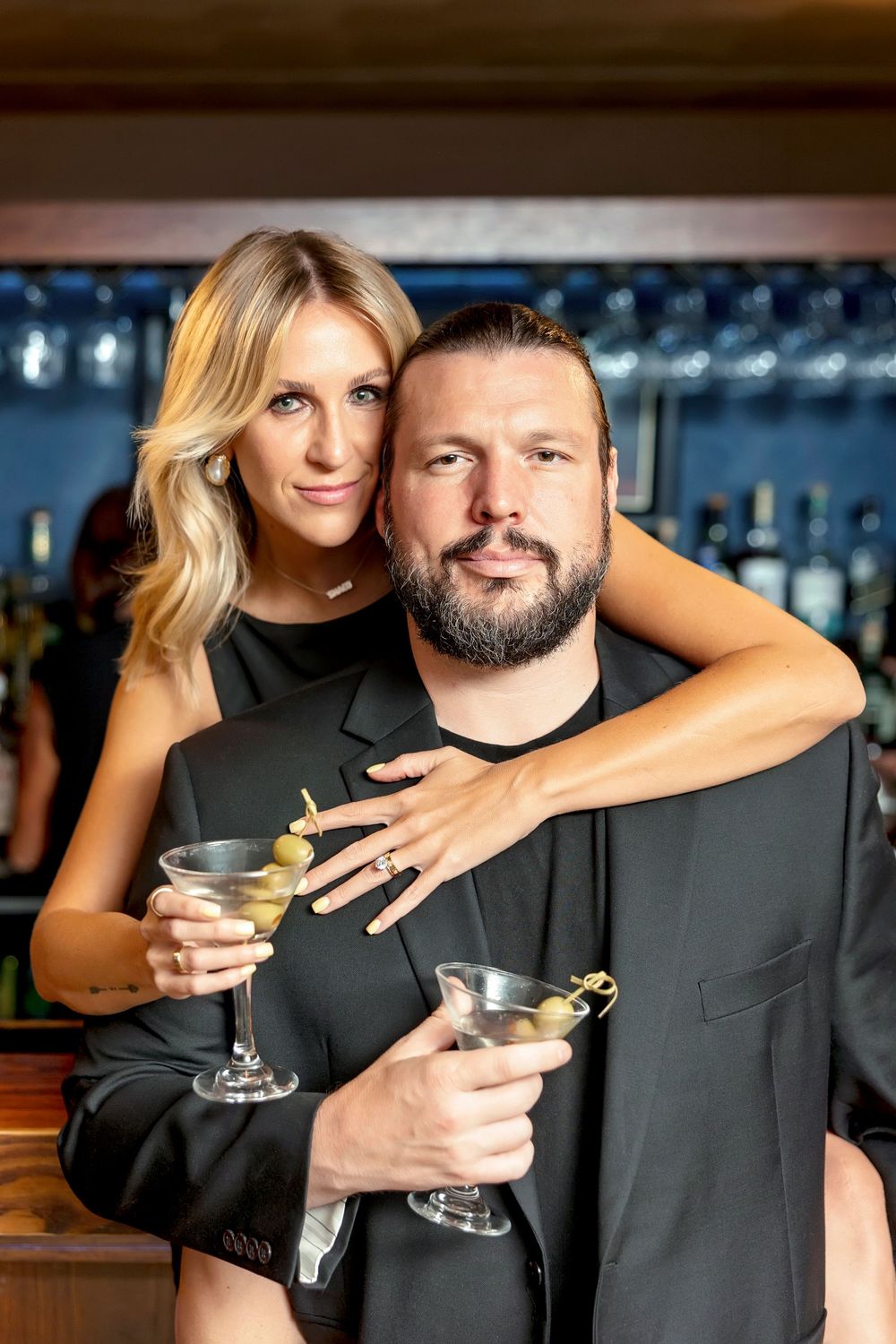 Couple in black attire poses with martini glasses at upscale bar. Dive bar engagement photos. engagement photos. clear lake wedding photo.