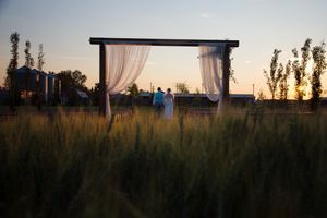 Framed by their wedding arch, bride and groom walk away from camera together into the sunset.