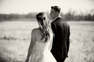Groom leads bride by the hand down a dirt path walking away from camera.