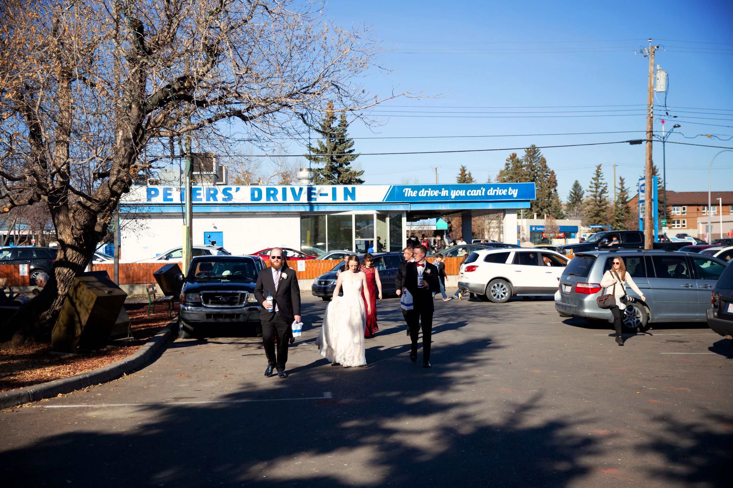 Bridal Party walks towards the camera with milkshakes and burgers away from a local drive in spot.