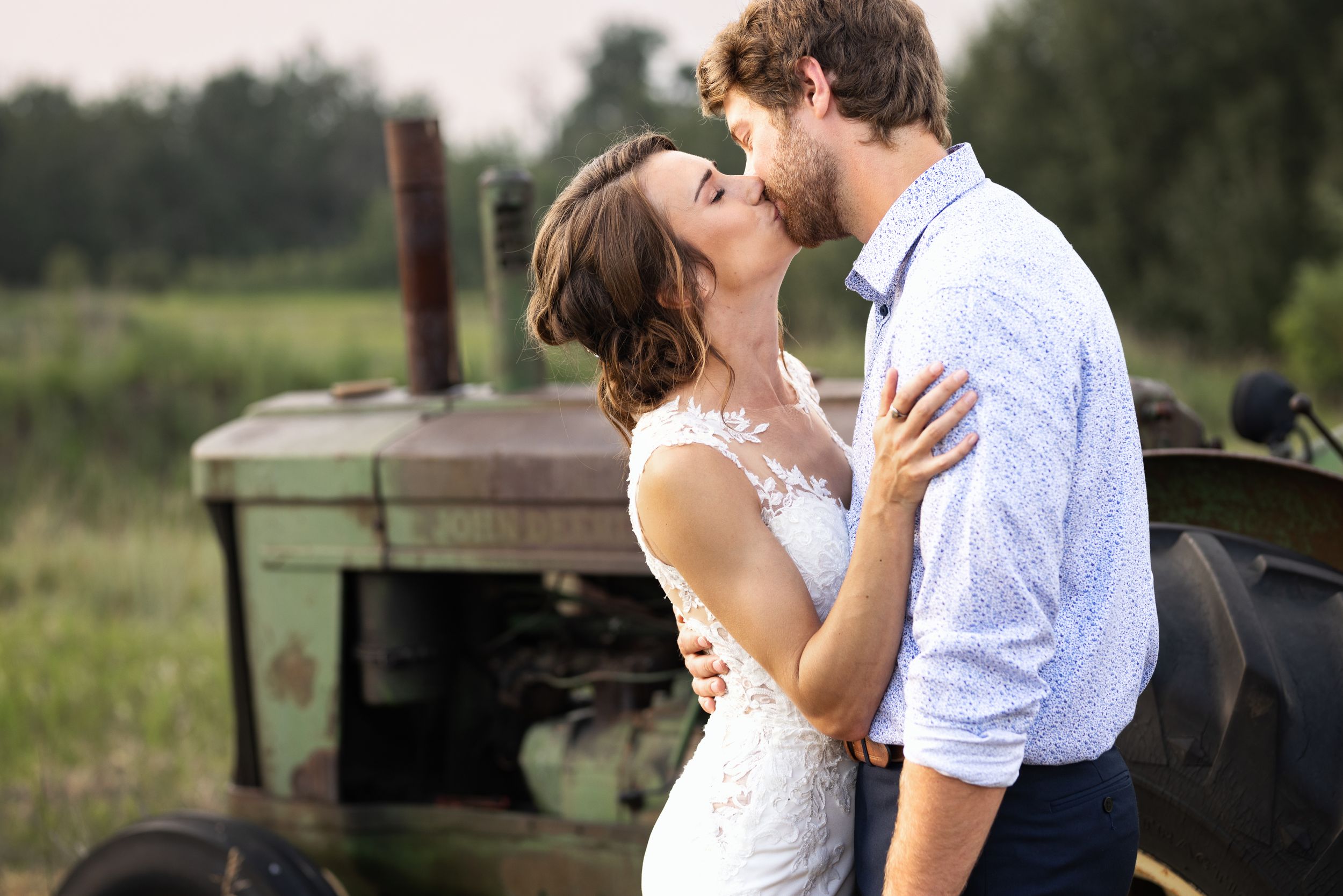 Bride and groom kiss in front of an antique tractor.