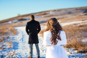 Groom faces away from camera in a snow covered park, bride walks up to him for their first look.